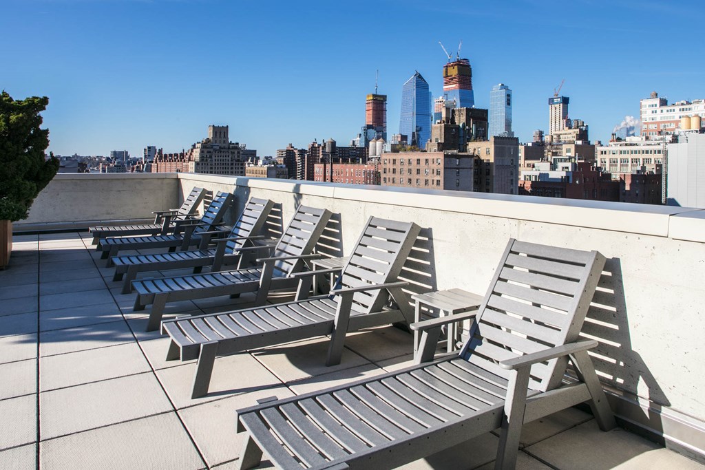 A row of sun loungers are on a roof terrace overlooking a city skyline.