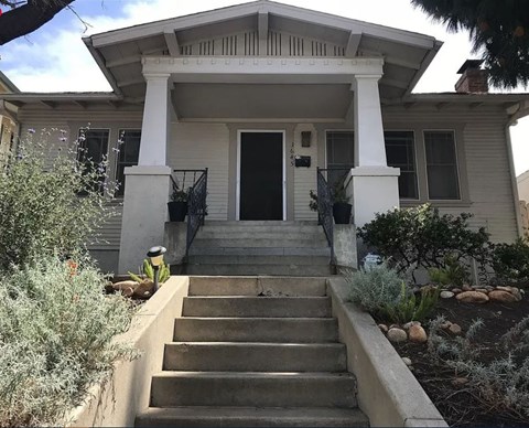 A white house with a black door and steps leading up to it.