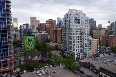 A cityscape with a large building in the foreground and a green mural on the side of a building.