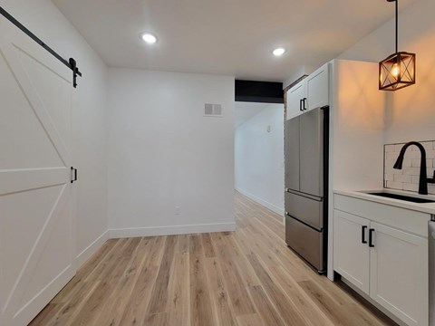 A kitchen with a refrigerator, cabinets, and a wooden floor.