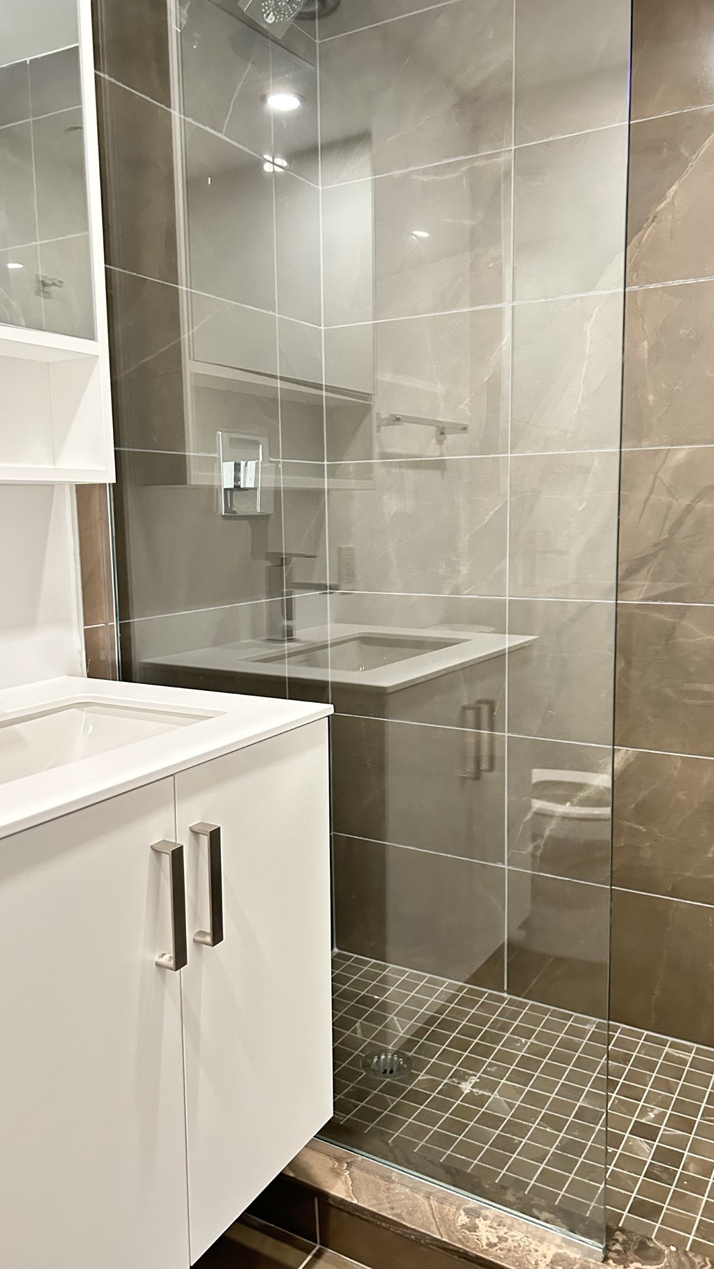 A white cabinet is in a bathroom with a glass shower door.