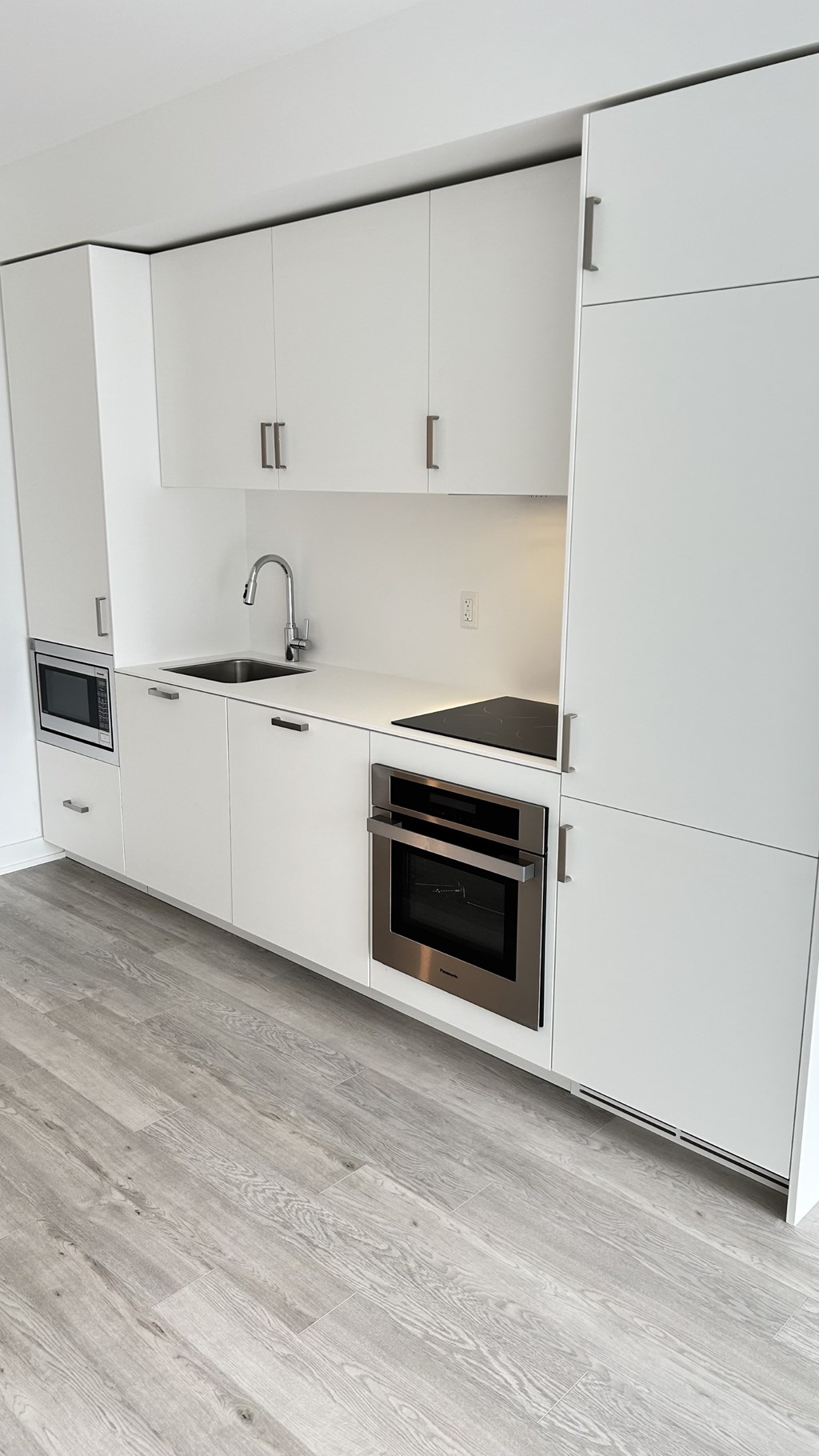 A modern kitchen with white cabinets and a wooden floor.