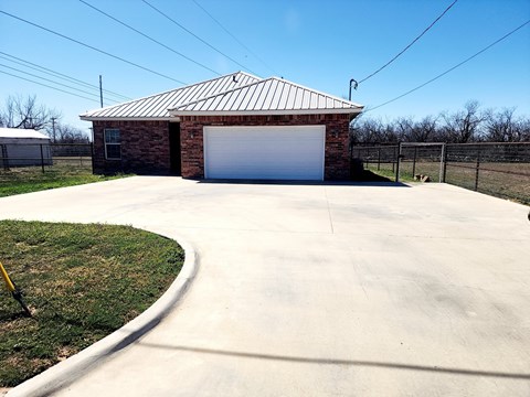 A garage with a metal roof and a white door is surrounded by a concrete driveway.
