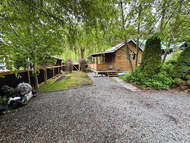 A gravel driveway leads to a wooden house with a deck.