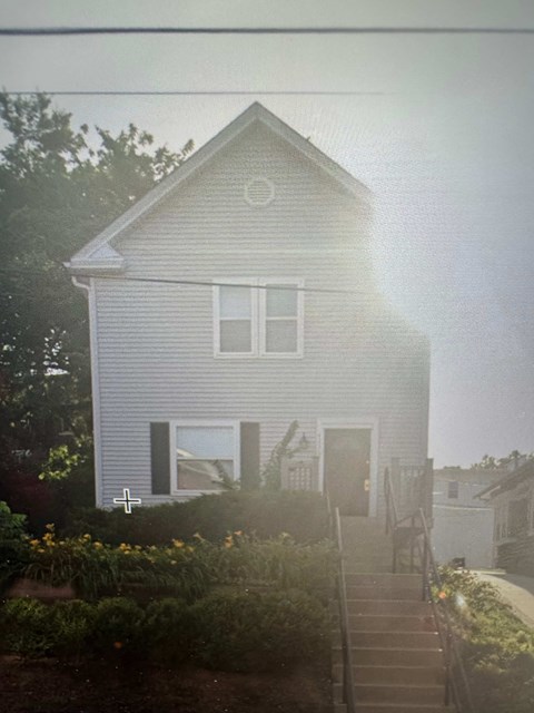 A house with a grey siding and a white door is surrounded by greenery.