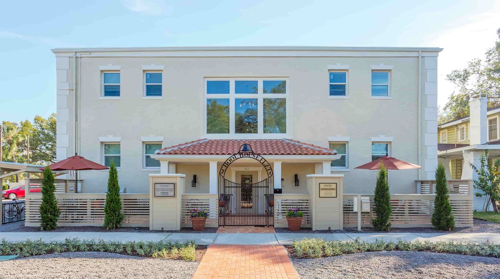 A beige house with a red roof and a brick pathway leading to the entrance.