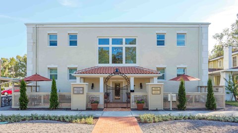 A beige house with a red roof and a brick pathway leading to the entrance.