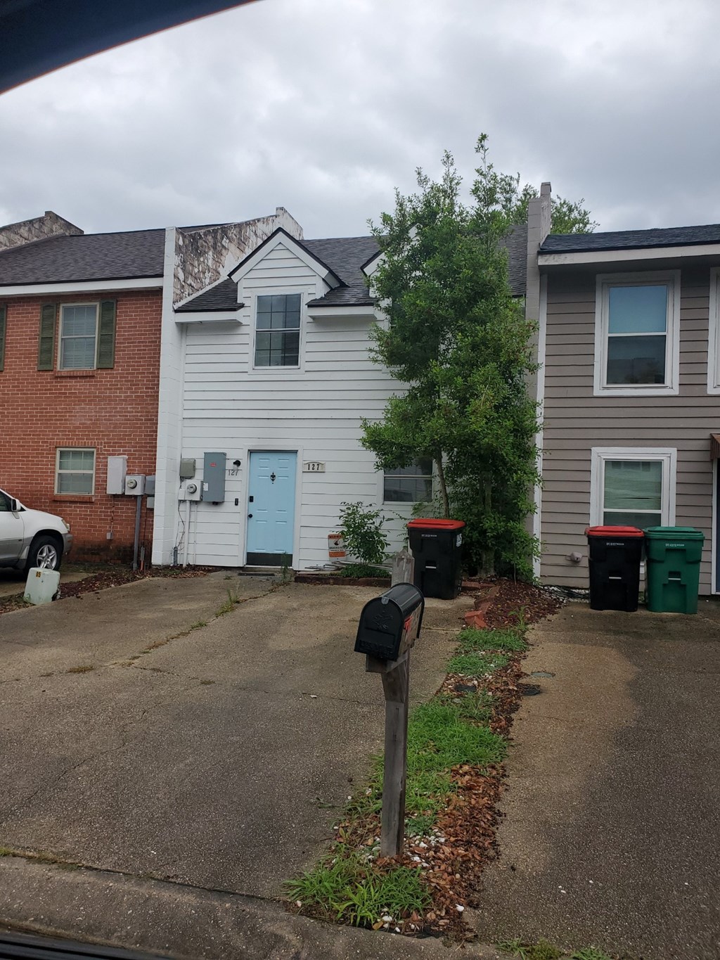 A grey house with a blue door is in front of a red brick house.