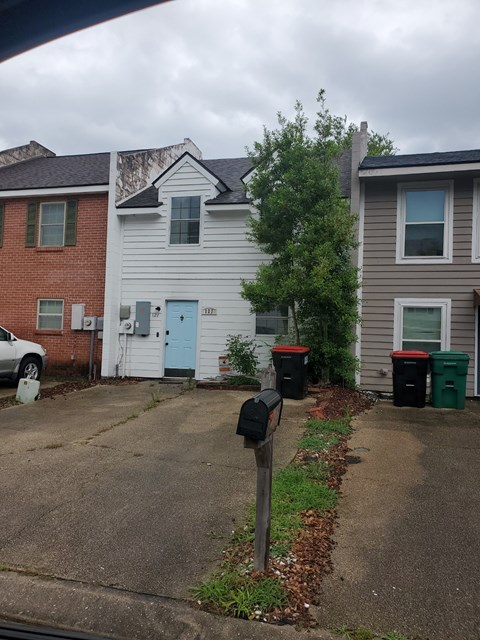 A grey house with a blue door is in front of a red brick house.