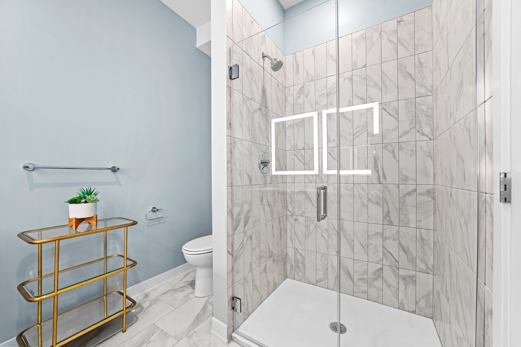 A bathroom with a marble tile shower and a gold shelf.