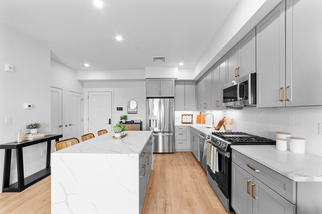 A modern kitchen with a white marble island and wooden floors.