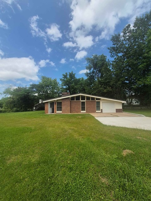 A house with a garage is situated in a grassy area.