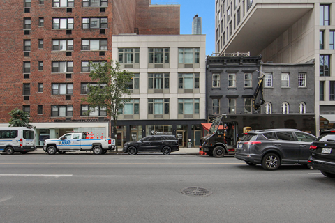 A black car is parked in front of a building with a white truck and a blue van behind it.