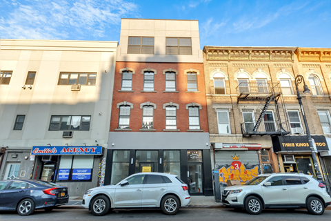 Cars parked in front of a row of buildings on a sunny day.