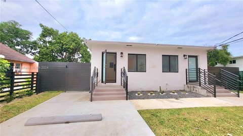 A house with a grey door and windows is surrounded by a black fence.