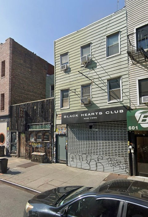 A car is parked on the street in front of a building with a Black Hearts Club sign.