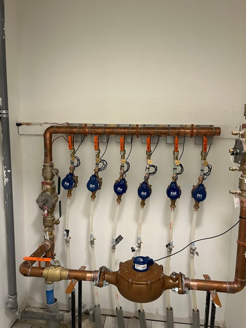 A wall of pipes and valves with orange and blue handles.