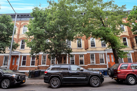 Two black SUVs parked on a street in front of a red brick building.