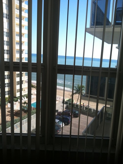 A view of the beach from a window with a car parked on the street.
