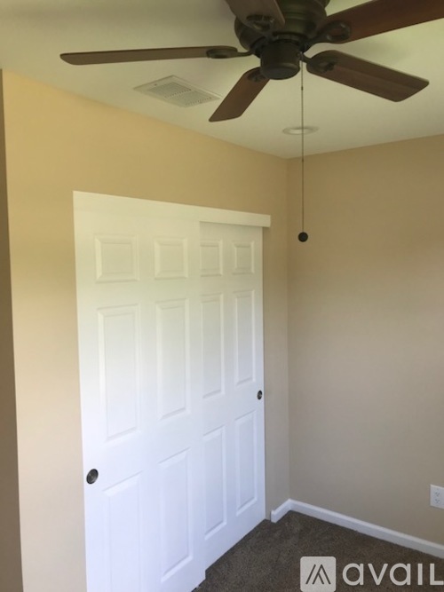 A room with a white door and a ceiling fan.