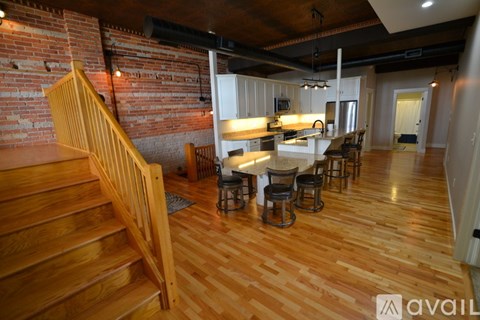 A wooden staircase leads to a kitchen with white cabinets and a dining table with chairs.