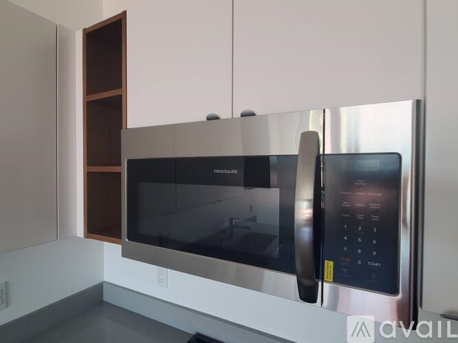 A stainless steel microwave with a digital display and control panel is mounted on a wall.