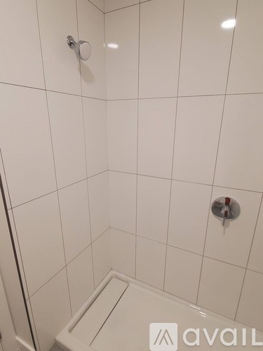 A white tiled shower stall with a drain and a shower head.