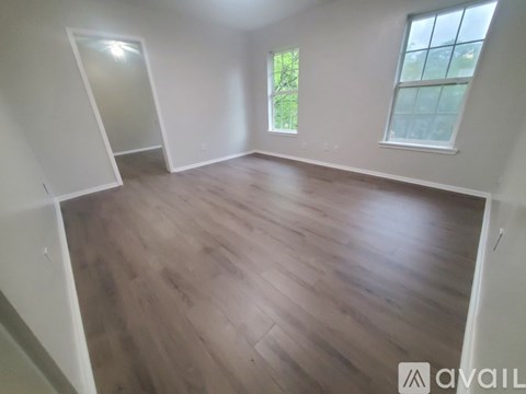 A room with wooden flooring and two windows.