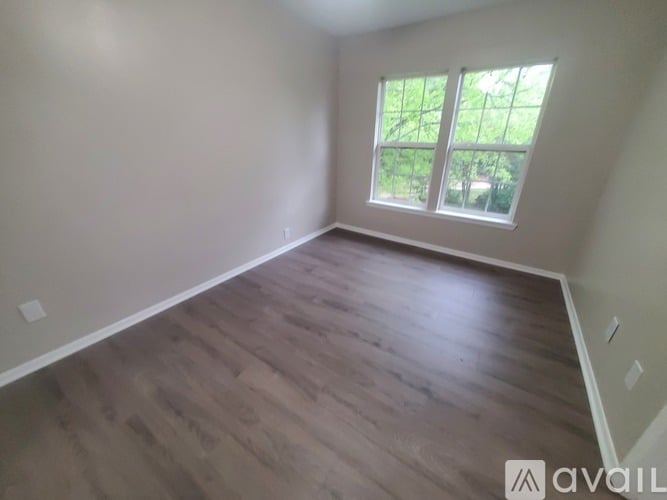 A room with wooden flooring and a window overlooking a green outdoor area.