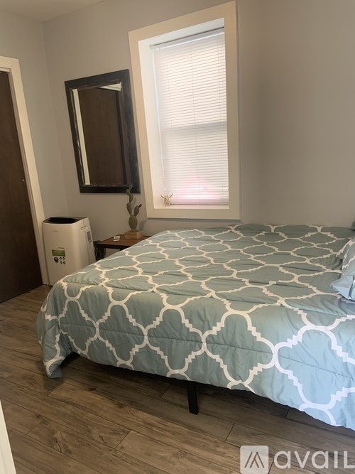 A bed with a blue and white patterned comforter sits in a room with a window and a mirror.