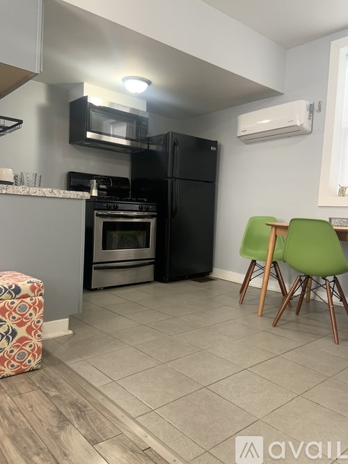 A kitchen with a black fridge, a green chair, and a patterned ottoman.