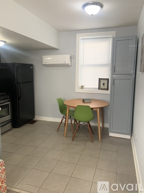 A kitchen with a black fridge, a table with two green chairs, and a window with blinds.