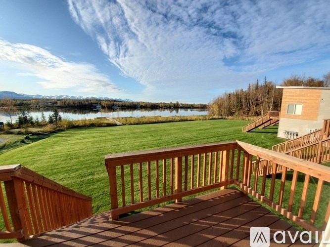 A wooden deck overlooks a grassy field with a lake and mountains in the distance.