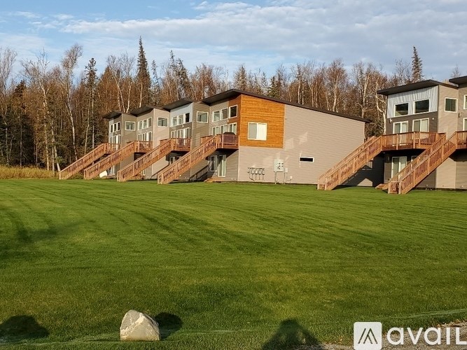 A large rock sits in the foreground of a grassy field with a building in the background.