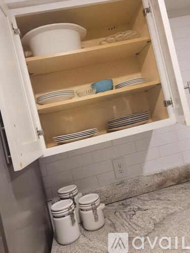 A kitchen cabinet is open, revealing plates and bowls inside.