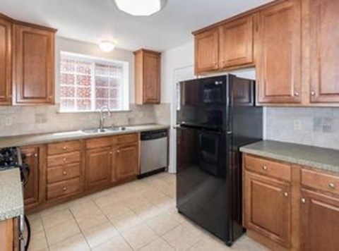 A black refrigerator is in a kitchen with wooden cabinets.