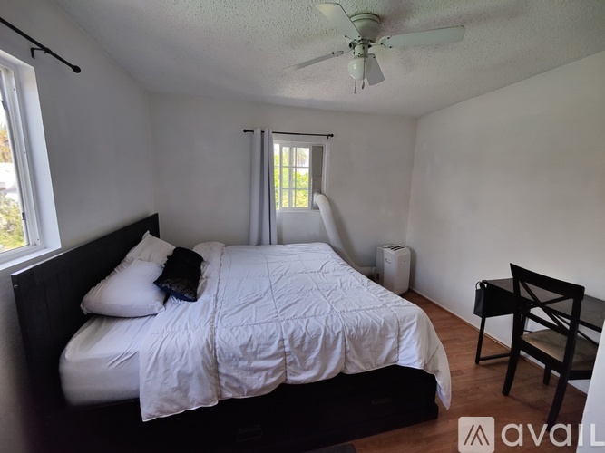 A bedroom with a bed, a nightstand, a window with curtains, and a wall hanging.