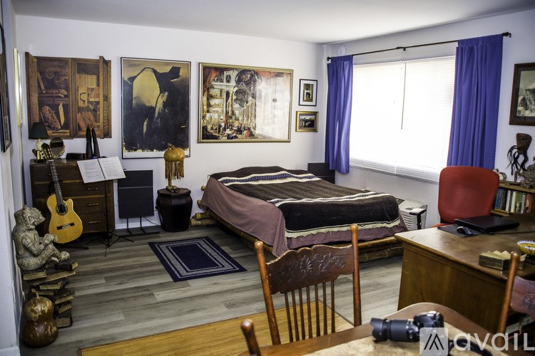 A bedroom with a bed, desk, chair, and guitar.