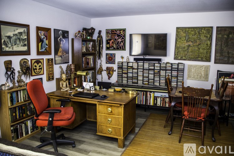 A room with a desk, chair, and bookshelf filled with various items.