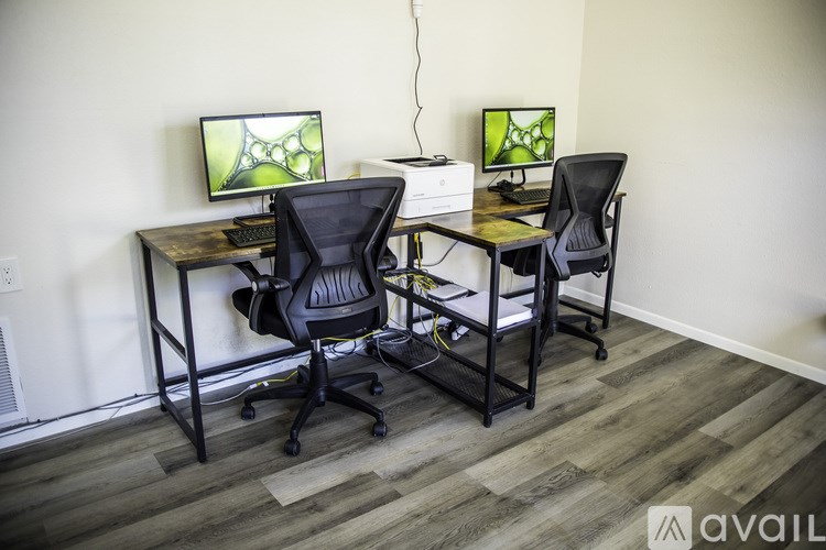 A room with a desk, two chairs, and two monitors.