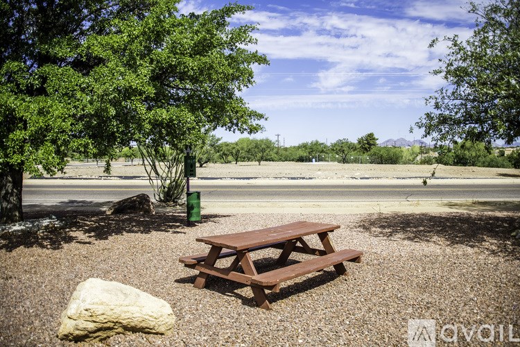 A picnic table sits in the middle of a gravel area with a tree to the left and a rock to the right.
