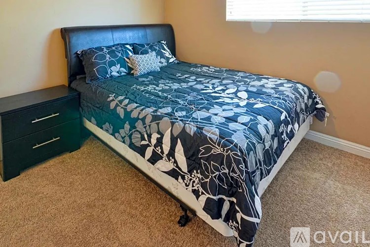 A bed with a dark headboard and a blue and white comforter is in a room with a carpeted floor.