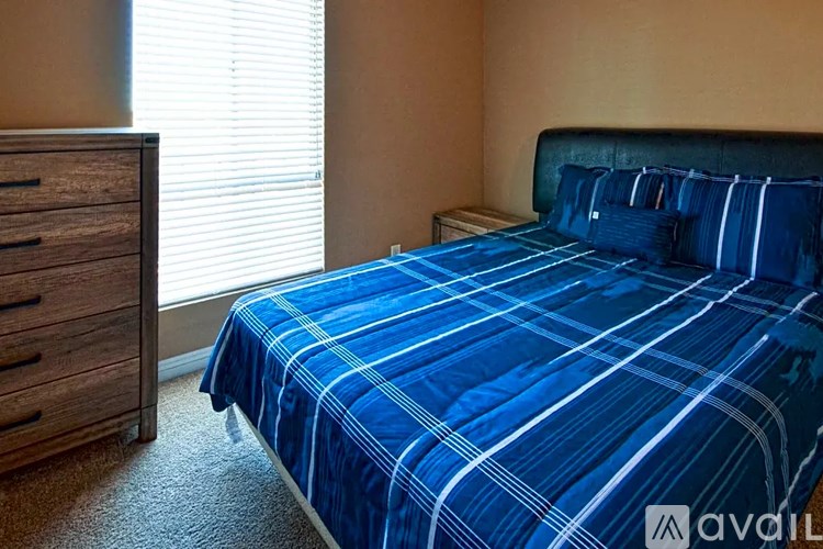 A bed with blue bedding and a wooden dresser beside a window.