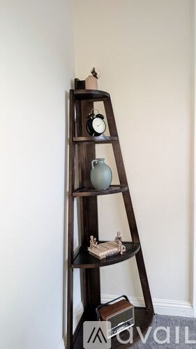 A wooden ladder shelf with a clock and a vase on it.