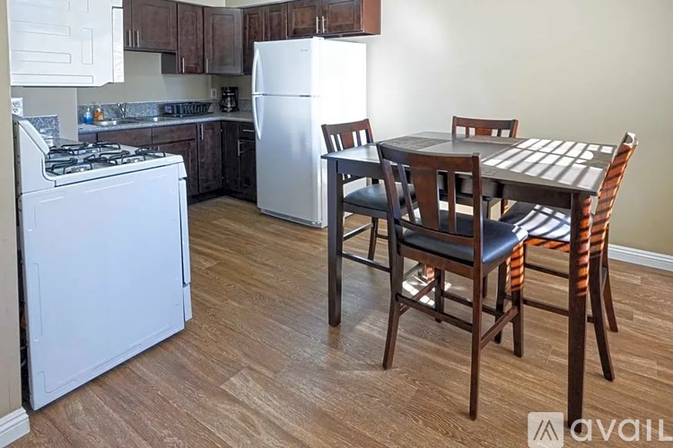 A kitchen with a white fridge and a dining table with chairs.