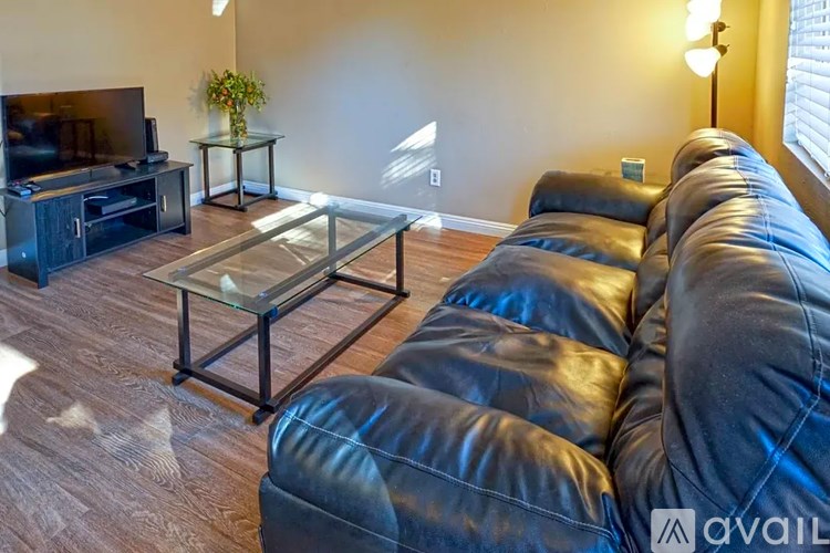 A living room with a glass coffee table and a black leather sofa.