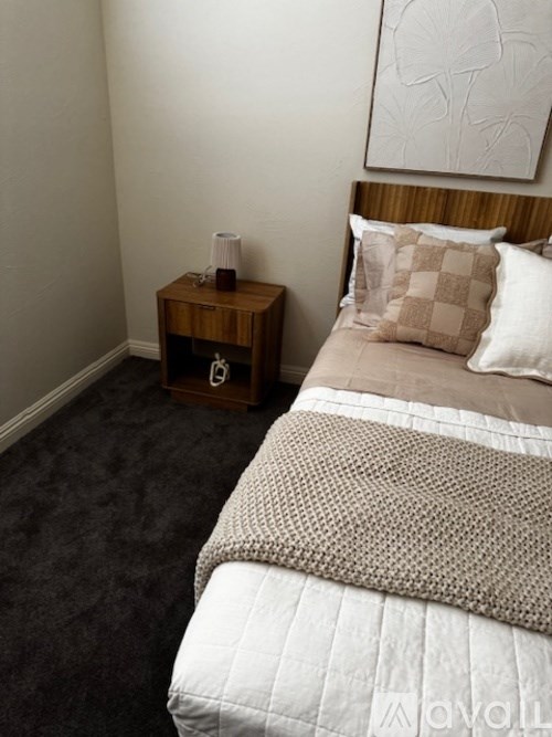 A bed with a white comforter and a wooden nightstand with a lamp on it.