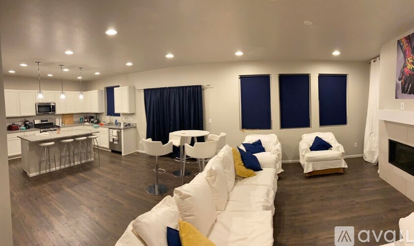 A living room with white furniture and a kitchen area in the background.