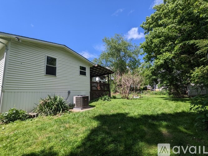 A house with a white siding and a brown roof is surrounded by green grass and trees.