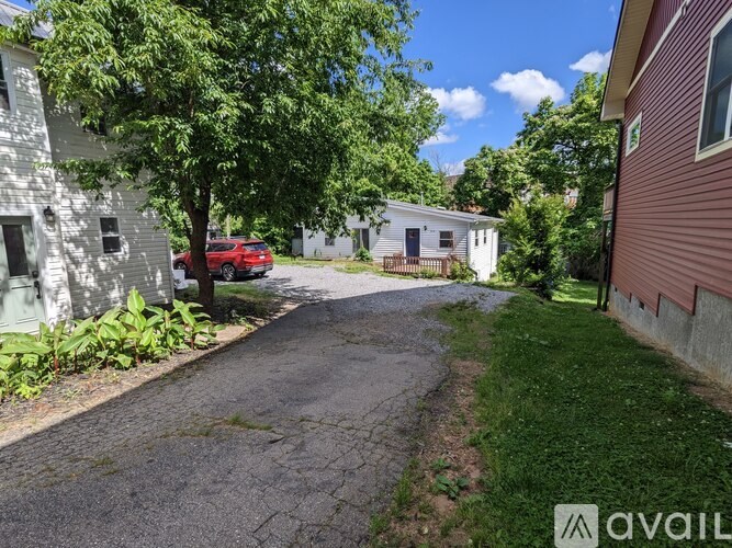 A red car is parked on a driveway in front of a white house.